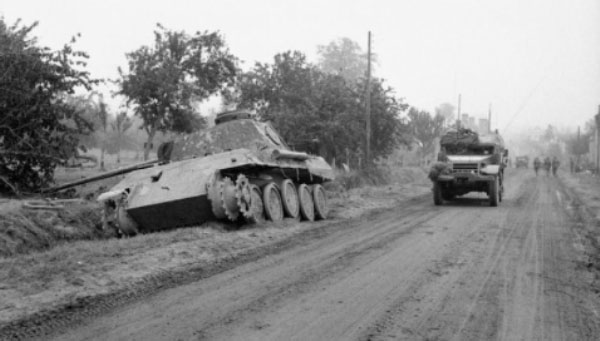 A Half-track Passes a Knocked-out German Panther Tank