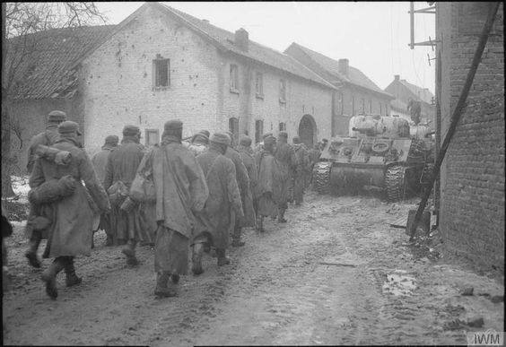 German prisoners trudge past a Sherman tank